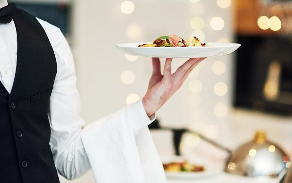 A professional waiter in a formal tuxedo and white shirt, expertly holding a plate of food, symbolizing high-quality service and professionalism in the hospitality sector